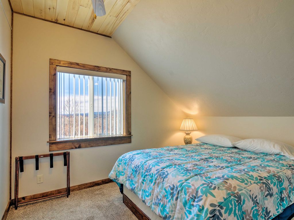 The second bedroom at Sunrise Hollow features a comfy queen bed, knotty aspen lined ceiling, and a ceiling fan, plus a panoramic view of the rim of Bryce Canyon in the distance.