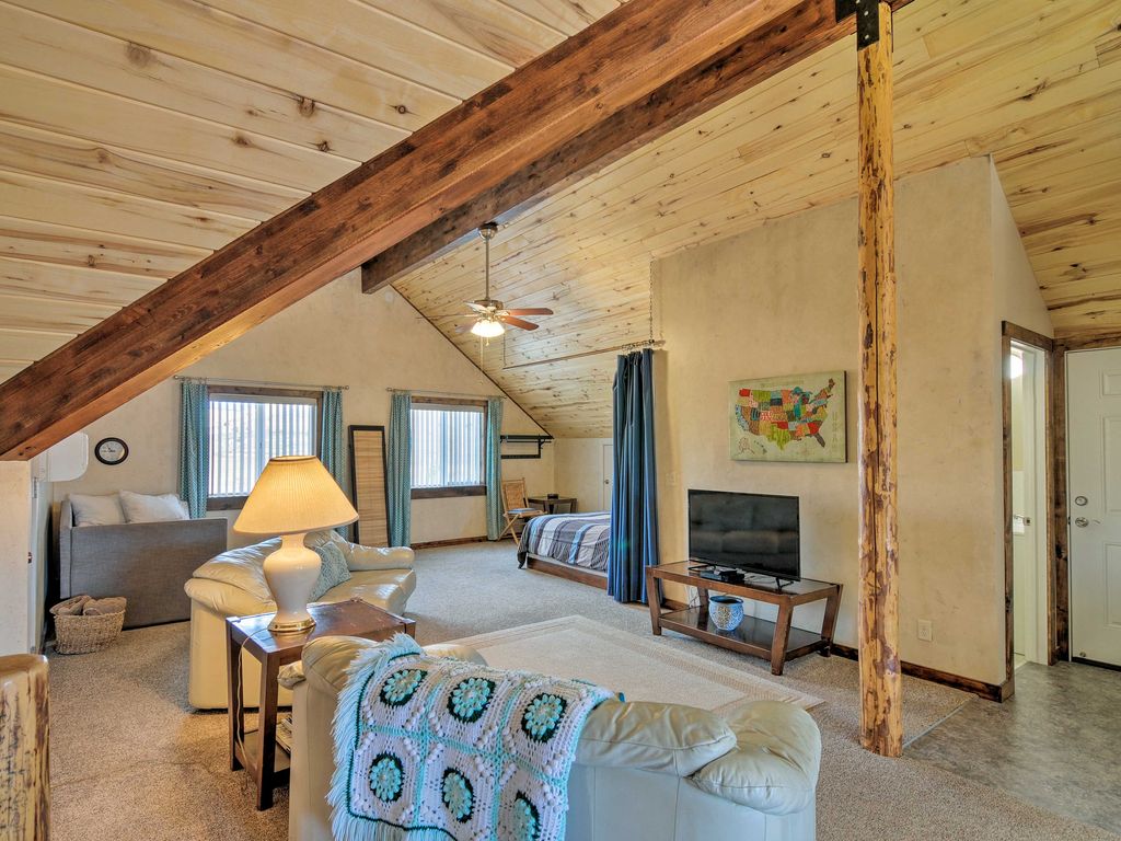 The spacious great room at Sunrise Hollow features leather couches, a flatscreen TV, and a sleeping nook with an extra queen bed! Notice the rustic cedar post and aspen-lined ceiling.